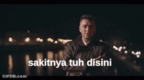 A Man Singing With The Words Sakitnya Tuh Disini Written Below Him GIF