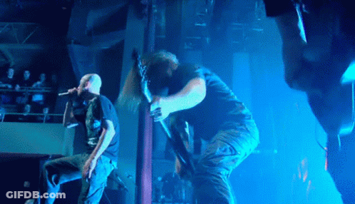 A Man Sings Into A Microphone While Another Man Holds A Guitar GIF
