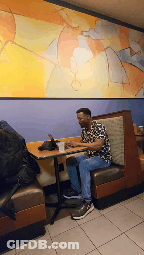 A Man Sits At A Booth In A Restaurant Using His Laptop GIF