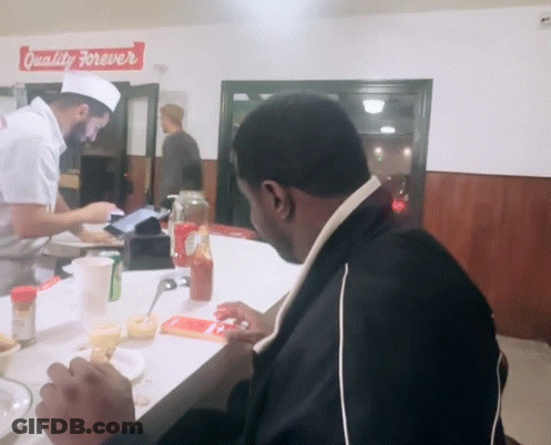 A Man Sits At A Counter In Front Of A Sign That Says " Quality Forever " GIF