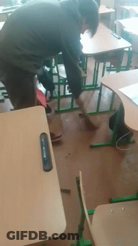A Man Sits At A Desk In A Classroom With A Cell Phone In His Hand GIF