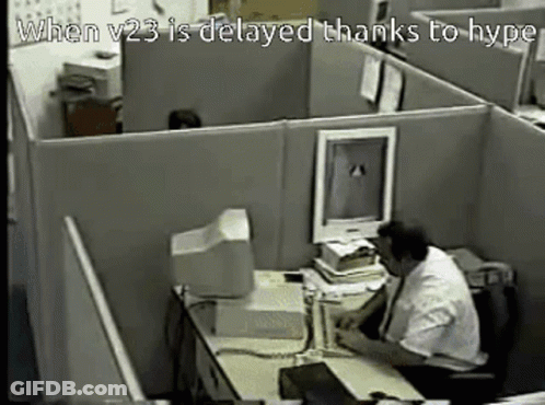 A Man Sits At A Desk In A Cubicle With The Words When V23 Is Delayed Thanks To Hype GIF