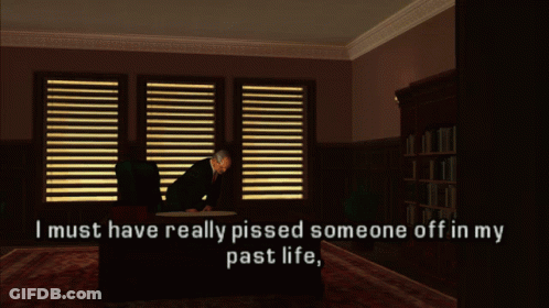 A Man Sits At A Desk In A Dark Room With The Words " I Must Have Really Pissed Someone Off In My Past Life " GIF