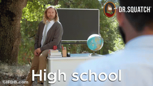A Man Sits At A Desk In Front Of A Blackboard With The Words High School On It GIF