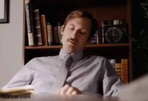 A Man Sits At A Desk In Front Of A Bookshelf With A World Book Atlas On It GIF