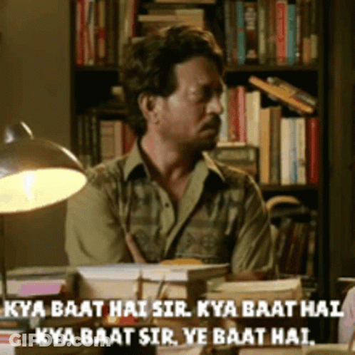 A Man Sits At A Desk In Front Of A Bookshelf With The Words Kya Baat Hai Sir Written On The Bottom GIF