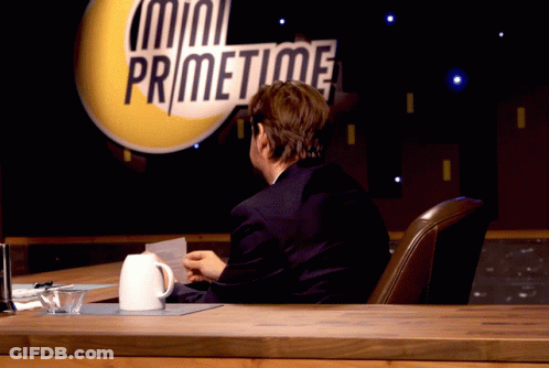 A Man Sits At A Desk In Front Of A Mini Primetime Sign GIF