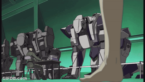 A Man Sits At A Desk In Front Of A Row Of Robots And A Person Standing Next To Them GIF