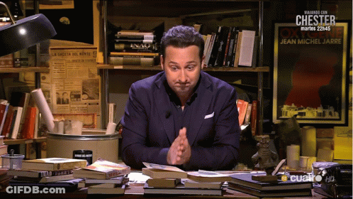 A Man Sits At A Desk In Front Of A Sign That Says Chester On It GIF