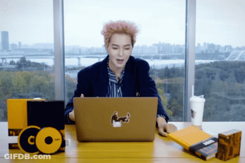 A Man Sits At A Desk Using A Laptop With A Sticker On It GIF