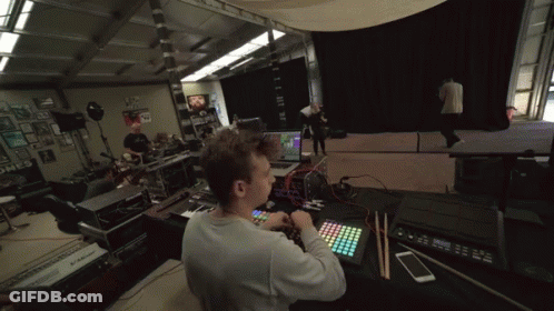 A Man Sits At A Desk With A Keyboard And A Phone In Front Of A Monitor That Says ' Korg ' On It GIF