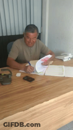 A Man Sits At A Desk Writing On A Piece Of Paper With A Pen GIF