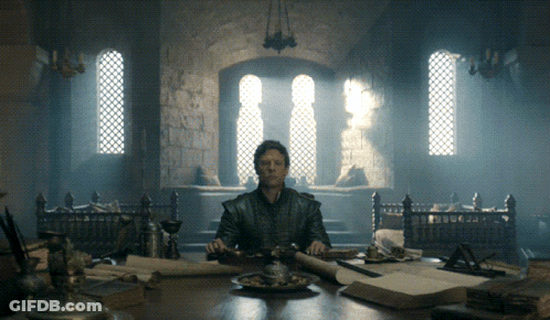 A Man Sits At A Table In A Dark Room With A Sword In His Hand GIF