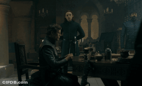 A Man Sits At A Table In A Dark Room With Candles GIF