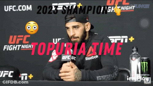 A Man Sits At A Table In Front Of A Ufc Fight Night Poster GIF