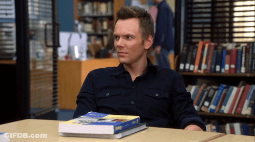 A Man Sits At A Table With A Book On Top Of It That Says ' Biology ' GIF