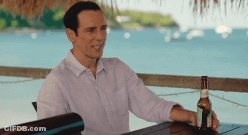 A Man Sits At A Table With A Bottle Of Beer In His Hand GIF