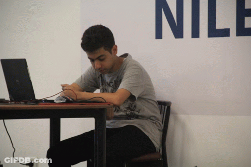 A Man Sits At A Table With A Laptop And A Mouse In Front Of A Wall That Says Nile GIF