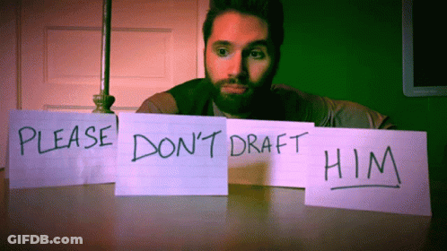 A Man Sits At A Table With A Sign That Says Please Do N't Draft Him GIF