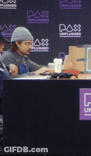 A Man Sits At A Table With A Watch Out Sign In Front Of Him GIF