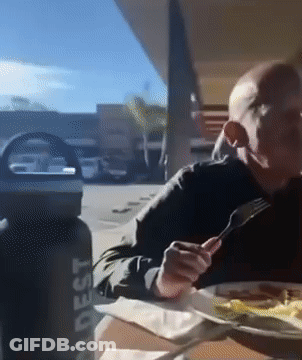 A Man Sits At A Table With A Water Bottle That Says ' Adest ' On It GIF