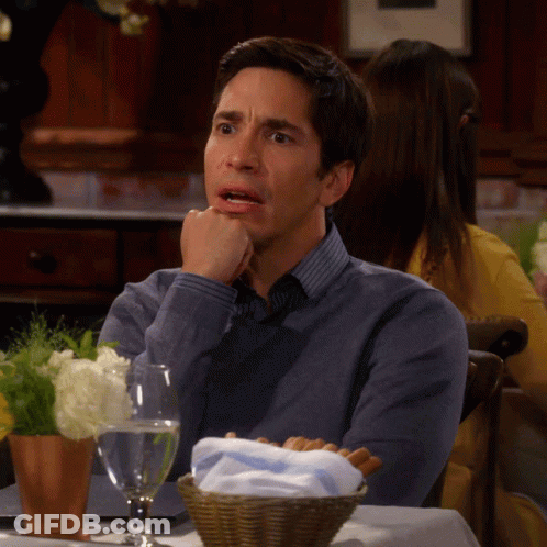 A Man Sits At A Table With His Hand On His Chin GIF