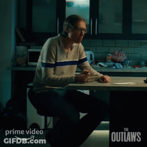 A Man Sits At A Table With The Words The Outlaws On The Bottom Right GIF