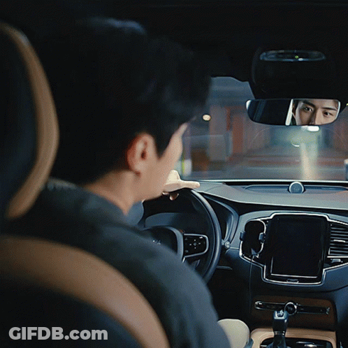 A Man Sits In A Car Looking At The Rear View Mirror GIF
