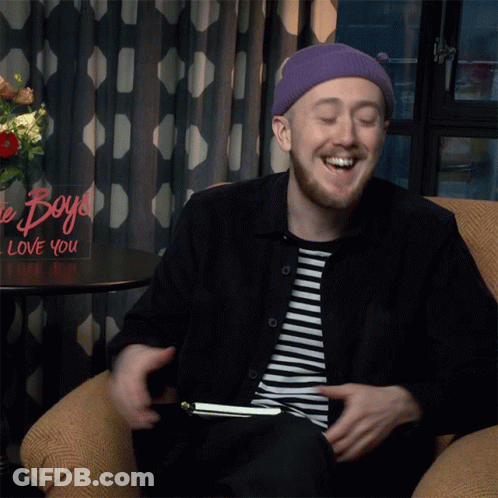 A Man Sits In A Chair In Front Of A Sign That Says Boys Love You GIF