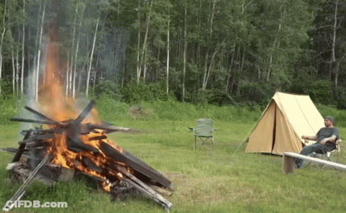 A Man Sits In A Chair Near A Campfire GIF