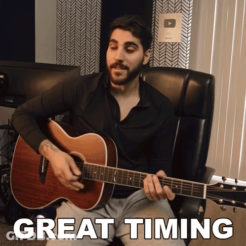 A Man Sits In A Chair Playing An Acoustic Guitar With The Words Great Timing Written Below Him GIF