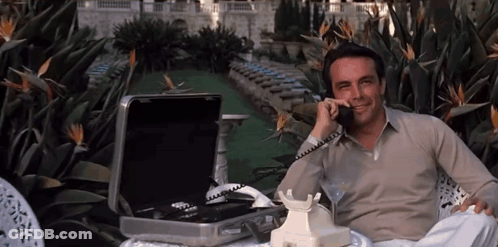 A Man Sits In A Chair Talking On A Phone GIF