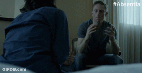 A Man Sits In A Chair Talking To A Woman With #Absentia On The Bottom Right GIF