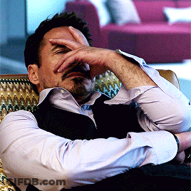 A Man Sits In A Chair With His Hand To His Face GIF