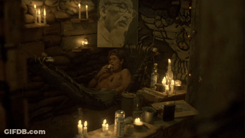 A Man Sits In A Dark Room With Candles And A Picture On The Wall GIF