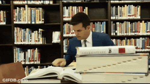 A Man Sits In A Library Surrounded By Books Including One Titled Shakespeare 8 GIF