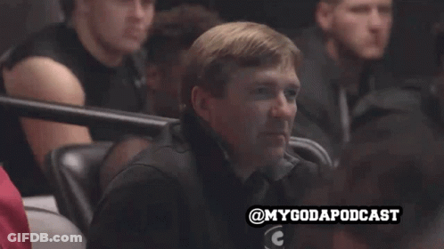 A Man Sits In A Stadium Watching A Game With The Hashtag Mygodapodcast GIF