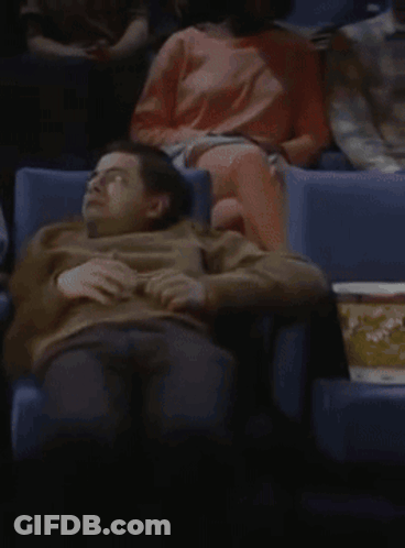 A Man Sits In A Theater With A Box Of Popcorn GIF