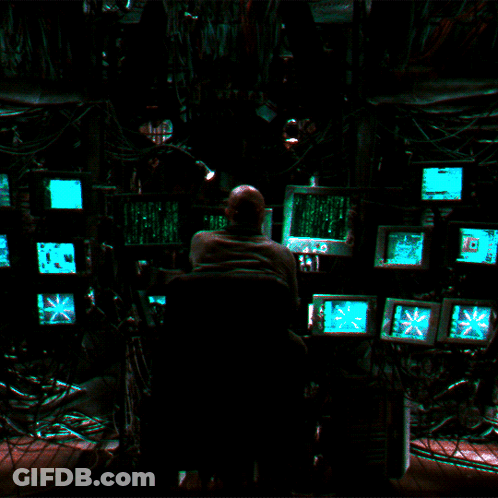 A Man Sits In Front Of A Bunch Of Computer Monitors Including One That Says ' Exit ' On It GIF