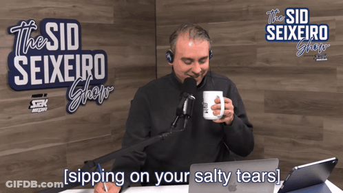 A Man Sits In Front Of A Microphone In Front Of A Sign That Says " The Sid Seixeiro Show " GIF