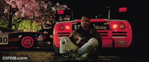 A Man Sits In Front Of A Red Car With The Number 40 On The Back GIF
