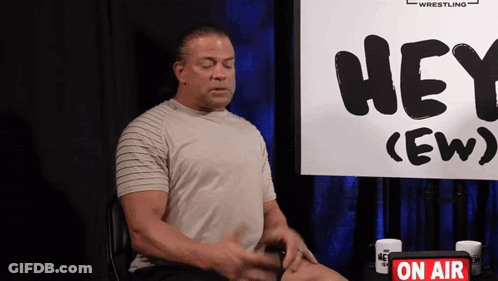 A Man Sits In Front Of A Sign That Says Hey Ew GIF