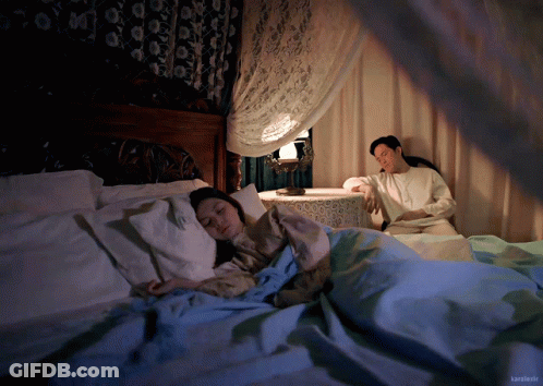 A Man Sits Next To A Woman Sleeping In A Bed With The Name Kamikaze On The Bottom Right Corner GIF
