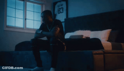 A Man Sits On A Bed In Front Of A Window With A Jersey On The Wall That Says 83 GIF
