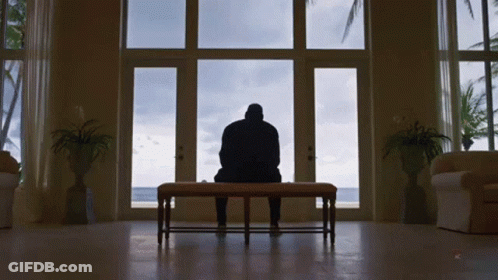 A Man Sits On A Bench In Front Of A Window Looking Out GIF