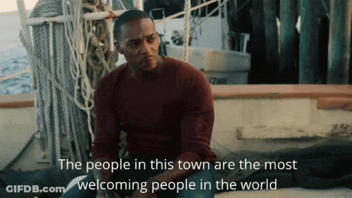 A Man Sits On A Boat With The Words " The People In This Town Are The Most Welcoming People In The World " Below Him GIF