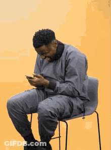 A Man Sits On A Chair Looking At His Phone GIF