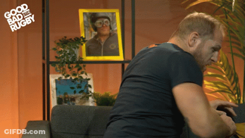 A Man Sits On A Couch In Front Of A Picture That Says Good Bad And Rugby On It GIF