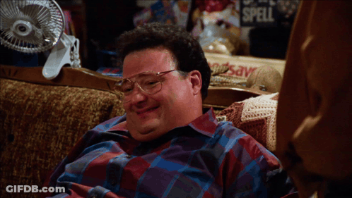 A Man Sits On A Couch Next To A Sign That Says " Spell " GIF