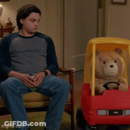 A Man Sits On A Couch Next To A Teddy Bear In A Cozy Coupe GIF